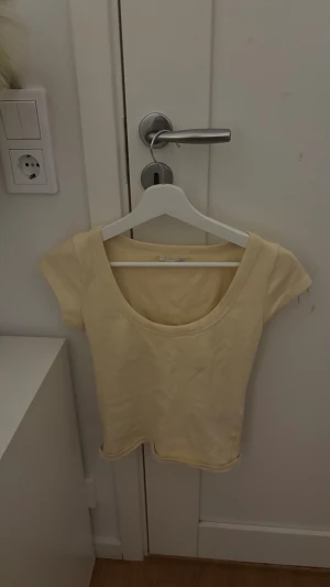 Ljusgul kortärmad topp - Säljer en ljusgul topp med rundad hals och korta ärmar. Enkel och stilren design som är lätt att matcha med olika outfits. Materialet känns mjukt och bekvämt mot huden, perfekt för varmare dagar. Passformen är normal och toppen har en klassisk look.