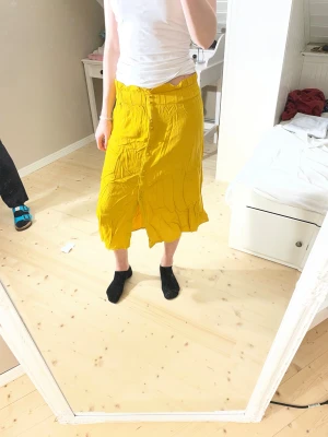 Gul långkjol från KIABI, strl 36 - Snygg senapsgul långkjol från KIABI i storlek 36. Kjolen har knappar framtill, resår i midjan och är tillverkad i 100% viskos. Den har en flowy känsla och passar perfekt för dig som gillar färgstarka plagg med enkel design. Modellen är 172cm lång.