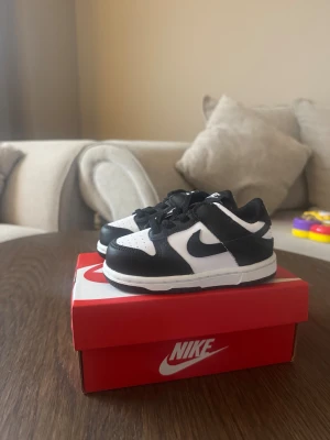 Nike Dunk Low svart/vit barn 22 - Nike Dunk Low sneakers i svart och vitt för barn. Klassisk låg modell med rund tå, snörning och platt sula. Snygg kontrast mellan svart och vit skinn, med perforerad tåbox och ikonisk Swoosh på sidan. Perfekt för dig som gillar streetstyle och vill ha något trendigt till vardags.