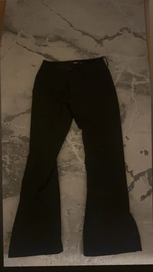 Svarta bootcut Vera kostymbyxor  - Snygga svarta kostymbyxor från bikbok i gamla Vera modellen med bootcut-snitt och klassisk design. Byxorna har låg midja och är tillverkade i ett slätt tyg som ger en stilren look. Har slut längst ner vid benen. Är i petit längd så passar dig som är runt 160cm. Perfekta för dig som gillar en tidlös och trendig siluett.