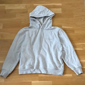 Tiger of Sweden Hoodie  - Säljer en stilren ljusgrå hoodie från Tiger of Sweden. Tröjan har huva med dragsko och diskret tryck på bröstet. Perfekt för en avslappnad och snygg look. Har ett litet hål på magen och en liten missfärgning vid halsen.
