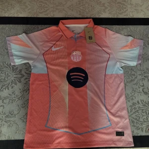 FC Barcelona Lamine Yamal Nike tröja M - Säljer en FC Barcelona fotbollströja från Nike i storlek M med Lamine Yamal och nummer 10 på ryggen. Tröjan har korta ärmar, krage och är i rosa och ljusblå toner med vita och mörkblå detaljer. Materialet är lätt och andas, perfekt för match eller träning.