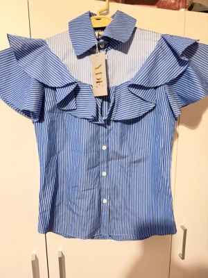 Blåvit skjorta  - Snygg blå och vit randig skjorta från YDE med stora volangdetaljer över axlarna och klassisk. Helt ny. Storlek S-M 