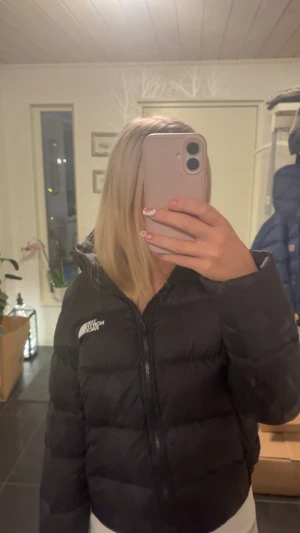 Svart dunjacka från The North Face - Säljer en svart dunjacka från The North Face med huva och dragkedja framtill. Jackan har en klassisk quiltad design, två fickor med dragkedja och logga på bröstet. Perfekt för kalla dagar när du vill hålla dig varm och se snygg ut. Kan gå ner i pris vid snabb affär.
