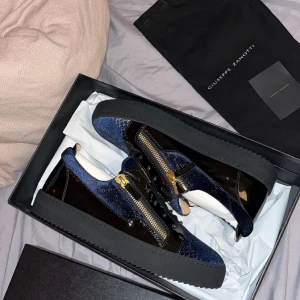Giuseppe Zanotti skor - ‼️Kvitto finns, Nypris: 6 495,00 Kr‼️ Snygga sneakers från Giuseppe Zanotti i mörkblå sammet och svart lack med guldfärgade dragkedjor på sidorna. Skorna har platt sula och rund tå, samt coola detaljer som ger en lyxig vibe. Perfekt för dig som gillar statement pieces och exklusiv design. Endast använda vid finare evenemang, topp skick. 