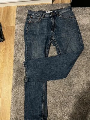 Blå jeans från 157 New Classic W33 L30 - Snygga blå jeans från 157 New Classic med klassisk femficksdesign och orangea sömmar. Modellen har rak passform och normal midja, tillverkade i slitstarkt denim. Perfekta för dig som gillar enkel och tidlös stil.