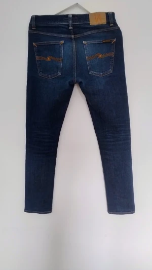 Nudie Jeans  W31 L34 - Snygga mörkblå slim fit jeans från Nudie Jeans med orange söm och broderad på bakfickorna. Modellen har fem fickor.