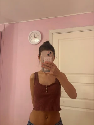 Mörk röd ribbad croppad linnetopp - Säljer en mörk röd croppad linnetopp med ribbad struktur och tre dekorativa knappar framtill. Toppen har breda axelband och en rundad halsringning, perfekt för dig som gillar en chill och enkel stil. Passar snyggt till jeans eller shorts.