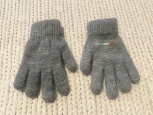 Grå stickade vantar  - Säljer ett par grå stickade vantar med ribbad mudd och klassisk femfingrad form. Diskret Pure Storage-logga på ena vanten. Mjukt och flexibelt material som håller händerna varma under kyliga dagar. Perfekt för dig som gillar enkel och stilren design.