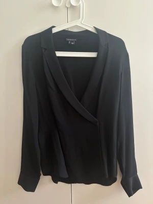 Svart omlott blus från Theory - Säljer en stilren svart omlott blus från Theory. Blusen är i 100 silke. Passar perfekt till byxor och kjol