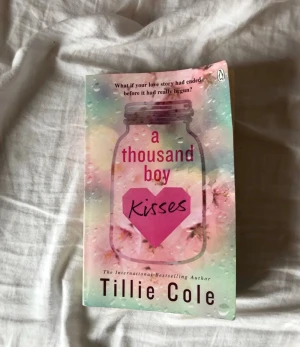 A Thousand Boy Kisses - En gripande och känslosam bok med ett romantiskt omslag, perfekt för dig som älskar starka kärlekshistorier. Omslaget har ett färgglatt, drömskt motiv med ett hjärta och texten 'What if your love story had ended before it had really begun?'.