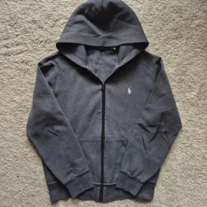 Ralph Lauren zip tröja i mörkgrå - hej säljer min mörkgråa Ralph Lauren tröja. Den är i storlek S . Den har Inga defekter alls förutom att tyget är lite slitet på några ställen och 1 litet hål vid armen!  Nypris: ca 2395 kr  Mitt pris: 799 kr  	•	Bredd (midja): 44 cm 	•	Ärmlängd: 60 cm 	•	Längd (från axel): 59 cm 	•	axelbrett : 47 cm Sitter lite stort på mig som är 168/169 cm så passar runt 170+ perfekt! Skriv vid minsta lilla fundering eller om du inte håller med om priset!