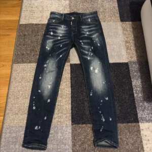 Dsquared2 slim jeans med splatter - Snygga blå jeans från Dsquared2 i slim fit med coolt splattermönster och slitningar framtill och baktill. Klassisk femficksmodell med gul kontrastsöm och logotypdetalj vid fickan. Tillverkade i jeansmaterial, perfekt för dig som gillar streetstyle.
