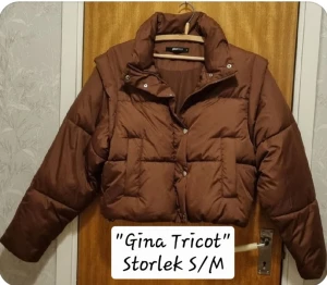 Brun pufferjacka från Gina Tricot - Säljer en brun pufferjacka från Gina Tricot i croppad modell. Jackan har hög krage, långa ärmar och knappar framtill. Perfekt för dig som gillar en trendig och varm look under kyliga dagar.