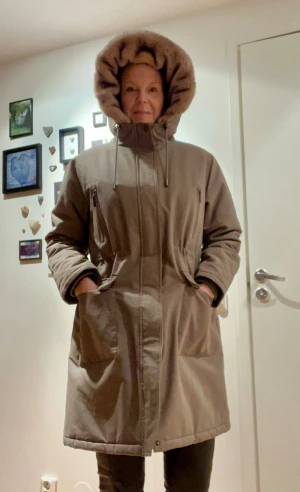 Beige parkas med fuskpäls och huva - Lexington Parkas för dam i storlek L. Jackan har huva med justerbar dragsko, flera praktiska fickor framtill inklusive dragkedjeförsedda och med knäppning. Midjan är justerbar för bättre passform. Materialet är bomull och plagget är avsett som övriga ytterkläder.  Man fryser aldrig i denna jacka.  Nypris ca 6500kr.   Mycket litet använd.  Finns i Hässelby villastad.