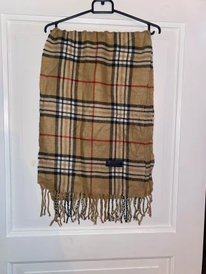 Beige Halsduk från Burberry - Beige halsduk från Burberry i 100% merinoull. Väldigt fint skick till ett bra pris. Mitt pris: 399kr
