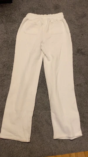 Vita mjukisbyxor med snörning - Säljer ett par vita mjukisbyxor med bred resår i midjan och snörning framtill. Byxorna har raka ben och stora fickor både fram och bak. Perfekta för chill dagar och riktigt sköna att ha på sig.