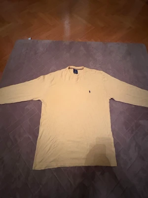 Gul långärmad tröja Polo Ralph Lauren - Snygg gul långärmad tröja från Polo Ralph Lauren i 100% bomull. Klassisk rund hals och diskret broderad logga på bröstet. Tröjan har en enkel och clean look, perfekt för dig som gillar stilrena plagg med lite färg.         Bra julklapp🔥                      (🔥om det syns några fleckar så är det sånt som går att tvätta 🧽 🔥) 