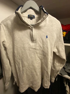 Beige half zip tröja Polo Ralph Lauren - Snygg beige långärmad tröja från Polo Ralph Lauren i storlek XL. Tröjan har en half zip-dragkedja vid halsen och ett blått broderat logomärke på bröstet. Materialet är mjukt och känns som bomull, perfekt för chill dagar.
