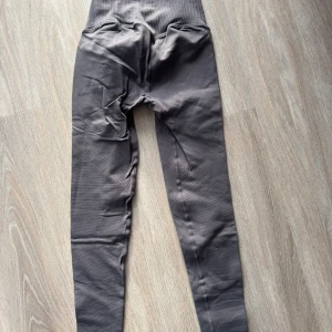 Grå ribbade leggings med hög midja - Snygga grå leggings med ribbad struktur och hög midja. De har ett tight passform och är tillverkade i ett stretchigt syntetmaterial som sitter skönt mot kroppen. Perfekta för träning eller chill, med coola detaljer längs benen som ger extra stil.