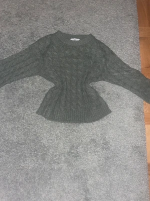 Mörkgrön stickad tröja med kabelmönster - Snygg mörkgrön stickad tröja med kabelstickat mönster och rund hals. Tröjan har långärmade ärmar och en figurnära passform vid midjan som ger en cool siluett. Perfekt för dig som gillar mysiga och trendiga plagg under kyliga dagar. Så mysig nu inför julen! Billigt pris!