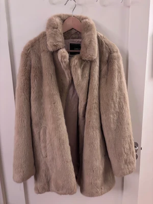 Beige pälsjacka från ONLY, stl L - Säljer en fluffig och mjuk beige pälsjacka från ONLY i storlek L. Jackan har klassisk krage, dolda knappar och sidofickor. Insidan är fodrad med glansigt tyg. Perfekt för dig som vill ha en varm och snygg look under kalla dagar.