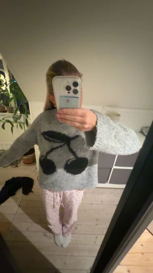 Grå stickad tröja med körsbärsmotiv - Supermysig grå stickad tröja med stort svart körsbärsmotiv på framsidan. Tröjan har en loose passform, rund halsringning och långa ärmar. Perfekt för dig som gillar en chill och trendig stil.