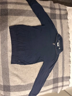 Marinblå half zip polotröja Jack & Jones - Snygg marinblå polotröja från Jack & Jones i storlek M. Tröjan har en stilren half zip-dragkedja vid halsen och är tillverkad i mjuk bomull. Långärmad modell med ribbad mudd vid nederkant och hals. Perfekt för dig som gillar enkel och clean stil.