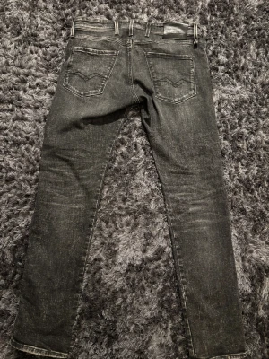 Replay Anbass svarta slim jeans - Snygga svarta Replay Anbass jeans i slim fit med klassisk femficksdesign och diskreta slitningar. Jeansen har raka ben och tydliga sömmar, tillverkade i stretchig denim för en bekväm passform. Perfekta för dig som gillar en stilren look.