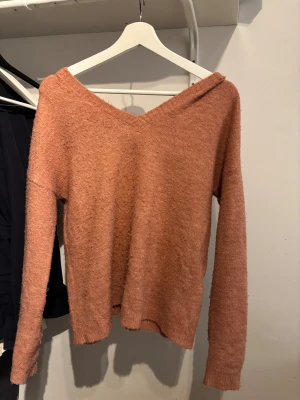 Rosa stickad V-ringad tröja Vero Moda - Mysig stickad tröja från Vero Moda i en varm rosa ton. Tröjan har V-ringad hals med svart spetsdetalj och långa ärmar. Materialet är fluffigt och mjukt, perfekt för kyliga dagar. Passformen är normal och modellen är enkel men ändå trendig. Den är lite sönder på axeln! Kolla på bilden. Skriv om du har frågor