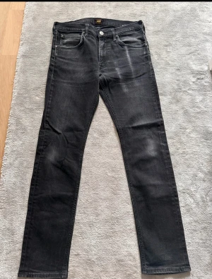 Svarta skinny jeans från Lee W30 L31 - Säljer ett par svarta skinny jeans från Lee med klassisk femficksdesign och diskret Lee-logga på bakfickan. Jeansen har en mörk tvätt med lätt slitning och raka ben. Perfekta för dig som gillar en smal passform och stilren look.