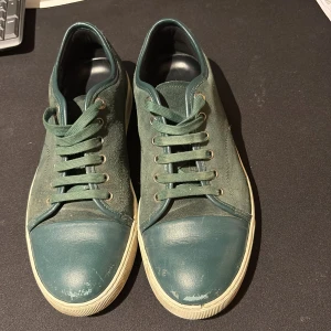 Gröna sneakers från Lanvin - Lanvin sneakers i mörkgrönt med snygga detaljer i mocka och skinn. Rund tå, platt sula och snörning framtill. Yttersulan är vit och har Lanvin-logga undertill. Perfekt för dig som gillar stilrena och exklusiva sneakers med en cool vibe.