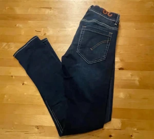 Mörkblå jeans från Dondup, storlek 29 - Snygga mörkblå jeans från Dondup, tillverkade i Italien. Klassisk femficksmodell med kontrastsömmar och raka ben. Jeansen har en stilren look med diskret logga i midjan och är gjorda i mjukt denimtyg som sitter skönt hela dagen. Priset är inte hugget i sten