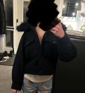 Marinblå teddyjacka med fuskpäls från Gina Tricot - Säljer en marinblå teddyjacka från Gina Tricot i storlek 158/164. Jackan är croppad med fluffig fuskpäls på kragen, har två stora bröstfickor och stängs med knappar framtill. Perfekt för dig som gillar mysiga och trendiga kappor.