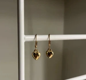 Guldiga örhängen med hjärtan - Snygga örhängen i guldton med hängande hjärtformade berlocker. Perfekta för att ge din look en söt och trendig touch. Passar dig som gillar stilrena och romantiska detaljer. Handgjort 