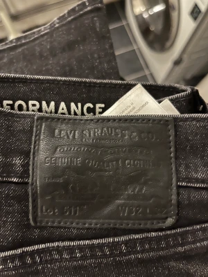 Levi's 511 svarta jeans W32 L32 - Svarta Levi's 511 jeans med klassisk femficksdesign och diskret röd Levi's-tag på bakfickan. Slim fit-modell med rak siluett, tillverkade i stretchigt jeanstyg för extra komfort. Perfekt för dig som gillar en stilren och modern look.