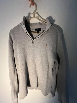 Grå half zip tröja från Polo Ralph Lauren storlek 18-20  - Säljer en stilren grå långärmad tröja från Polo Ralph Lauren med half zip och broderad logga på bröstet. Tröjan är i mjuk bomull och har en klassisk passform som funkar till allt. Perfekt för lager-på-lager under hösten och vintern.