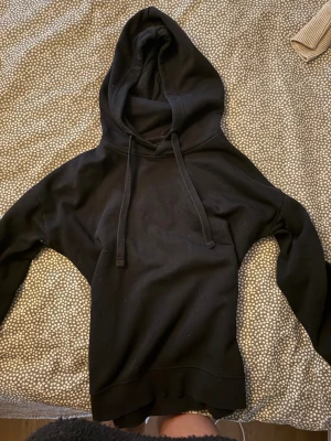 Svart hoodie från 157, storlek S - En klassisk svart hoodie från 157 med huva och snörning. Tröjan har en relaxed passform och är tillverkad i mjuk bomullsmix, perfekt för chill dagar. Långa ärmar och ribbade muddar ger en skön vibe.