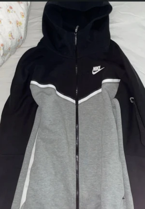 Nike hoodie svart och grå S - Nike hoodie i storlek S med svart och grå färgblock, vit Nike-logga på bröstet och hel dragkedja framtill. Tröjan har huva och långa ärmar, samt en vit detaljlinje över bröstet. Perfekt för chill eller träning. Dragkedjan vid armen har en liten lufsig bit men går att fixa det är inga problem 