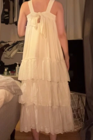 Vit långklänning med volanger och knyt - Säljer en superfin vit långklänning med breda axelband och knyt i ryggen. Klänningen har flera lager volanger och broderade detaljer längst ner. Perfekt som en längre studentklänning eller en snygg klänning till resan bort i värmen i vinter!  Köpt för 900 kr på Nelly i somras använd 1 gång.går ned till anklarna på mig ungefär som är 160 cm lång.   