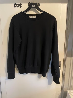Svart Stone Island sweatshirt - Svart sweatshirt från Stone Island. Tröjan har den ikoniska Stone Island-loggan på vänster ärm, fäst med två knappar. Materialet är mjuk bomull och passformen är normal, perfekt för en clean och stilren look. Kan gå ner i pris vid snabb affär Mvh