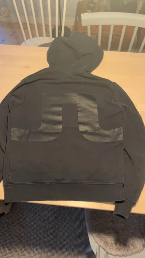 Svart hoodie från J.Lindeberg S - Svart hoodie från J.Lindeberg i storlek S. Tröjan har en stor huva med snörning, magficka och ett stort, blankt J.Lindeberg-tryck på ryggen. Mjuk bomullskänsla och ribbade muddar vid ärmar och nederkant. Perfekt för chill och streetwear. Lite tvättpåverkad.