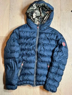 Colmar pufferjacka vändbar camo/marin - Säljer en vändbar pufferjacka från Colmar med ena sidan i marinblått och andra i camouflage. Jackan har huva, dragkedja och två fickor med zip.  Storlek large