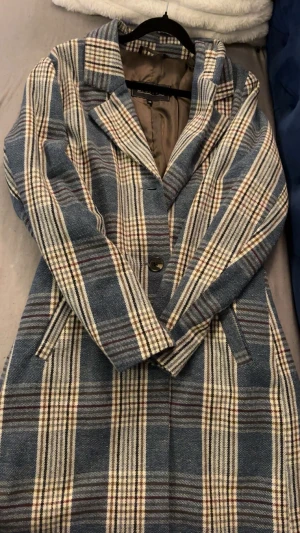 Blårutig kappa från Giovanna - Säljer en snygg blårutig kappa från Giovanna i storlek 48. Jackan har klassisk krage, knäppning med knappar och två fickor framtill. Materialet är tjockt och känns som ullblandning, perfekt för kyliga dagar. Rutig design i blått, beige och brunt ger en cool vintage vibe.