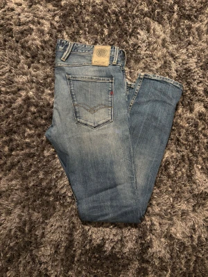 Replay jeans - Snygga blå jeans från Replay i klassisk slim fit i ljusare tvätt. Modellen har fem fickor, kontrastsömmar och Replay-logga på fickan. Jeansen är tillverkade i bomull och har knapp och dragkedja i gylfen. Endast en liten defekt i skrevet(se sista bild) 