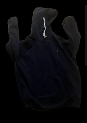 Mörkblå hoodie från Polo Ralph Lauren - Säljer en mörkblå hoodie från Polo Ralph Lauren med vit snörning i huvan och rött broderat logomärke på bröstet. Tröjan har en klassisk känguruficka och långa ärmar, perfekt för chill dagar. Passar dig som vill ha en stilren stil.  (Skriv för mer bilder)