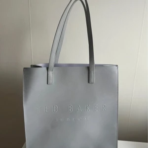 Grå shoppingväska från Ted Baker - Ted Baker handbag  Description  Grå Ted Baker shoppingväska  Ted Baker  Endast använd ett fåtal gånger.  Höjd 34 cm  Bredd 34 cm  Djup 9 cm