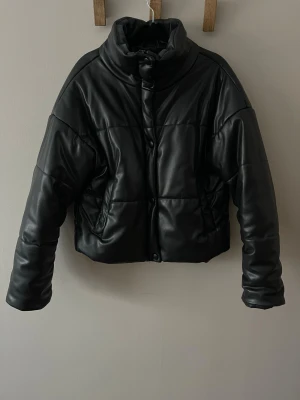 Svart pufferjacka från NA-KD - Säljer en superfin svart pufferjacka från NA-KD med hög krage och croppad passform. Säljer då den tyvärr inte kommer till användning längre