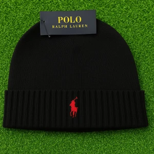 Svart ribbad mössa från Polo Ralph Lauren - Svart mössa från Polo Ralph Lauren med ribbad kant och röd broderad logga framtill. Stilren och enkel design som passar perfekt för kalla dagar. Materialet är mjukt och bekvämt, och mössan har en klassisk form som sitter snyggt på huvudet.
