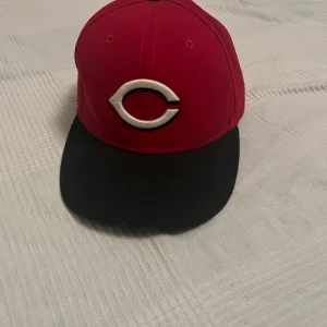 Röd Cincinnati Reds keps från New Era - Snygg röd keps från New Era 59FIFTY med svart skärm och broderad Cincinnati Reds-logga framtill. MLB-märke baktill och klassisk passform. Perfekt för dig som gillar baseball eller vill ha en sportig streetstil.